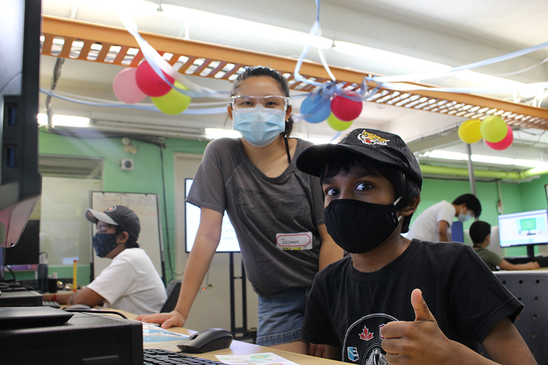 Computer lab summer camper giving thumbs up next to a counsellor, both are masked.